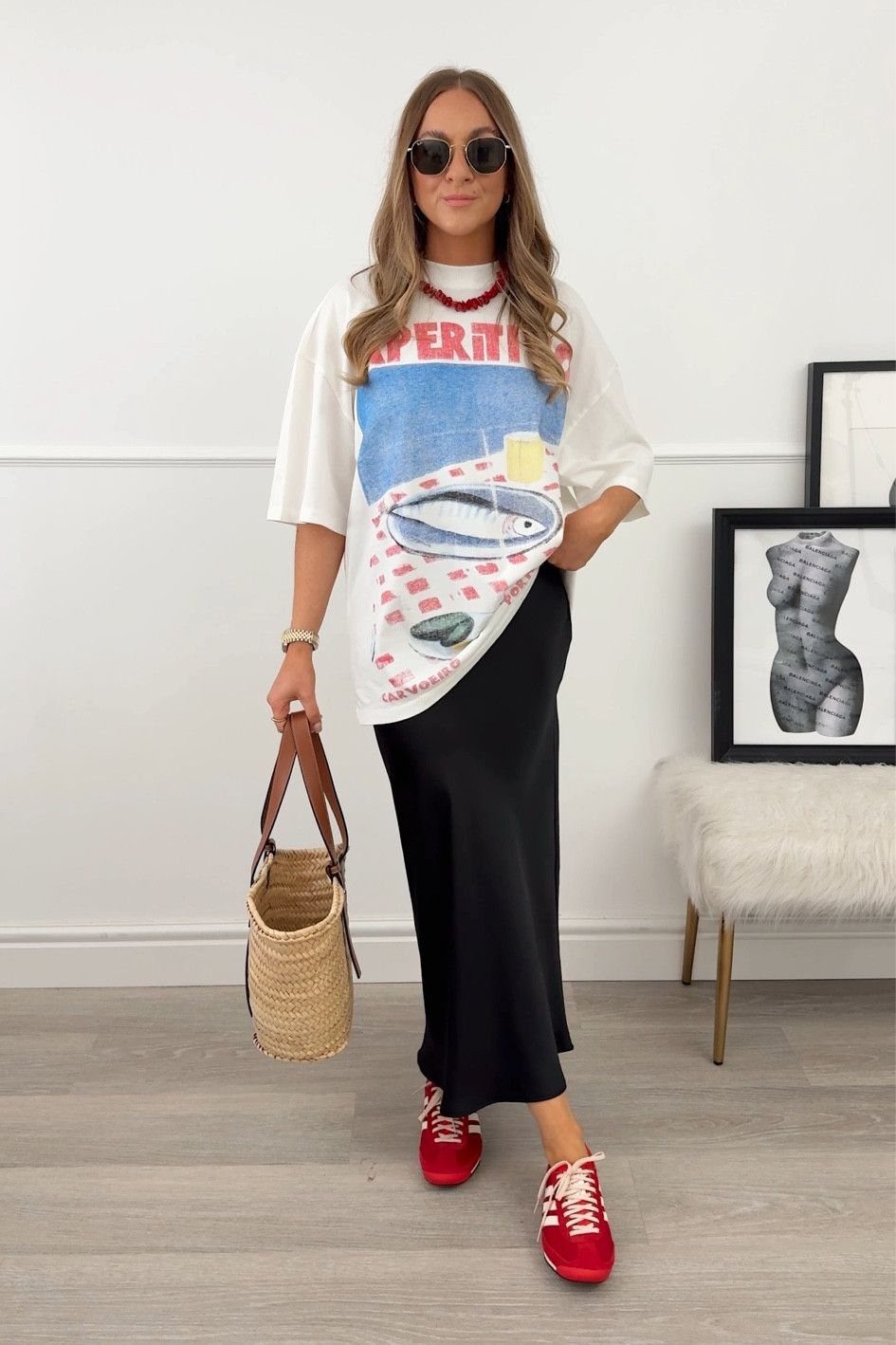 Woman posing in an oversized graphic t-shirt, long black satin skirt, and red sneakers.
