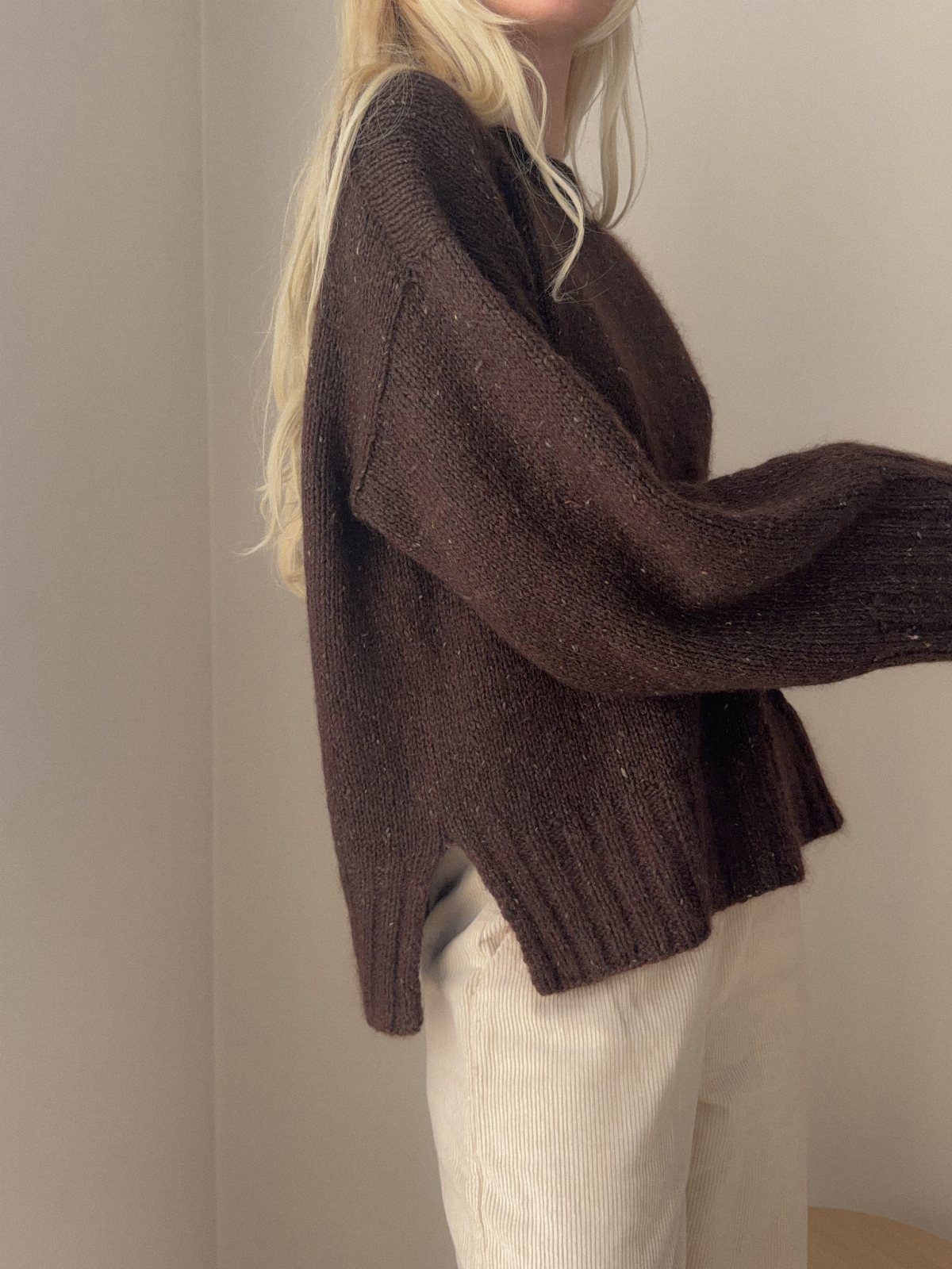 A person wearing an oversized dark brown chunky knit sweater and cream corduroy pants.