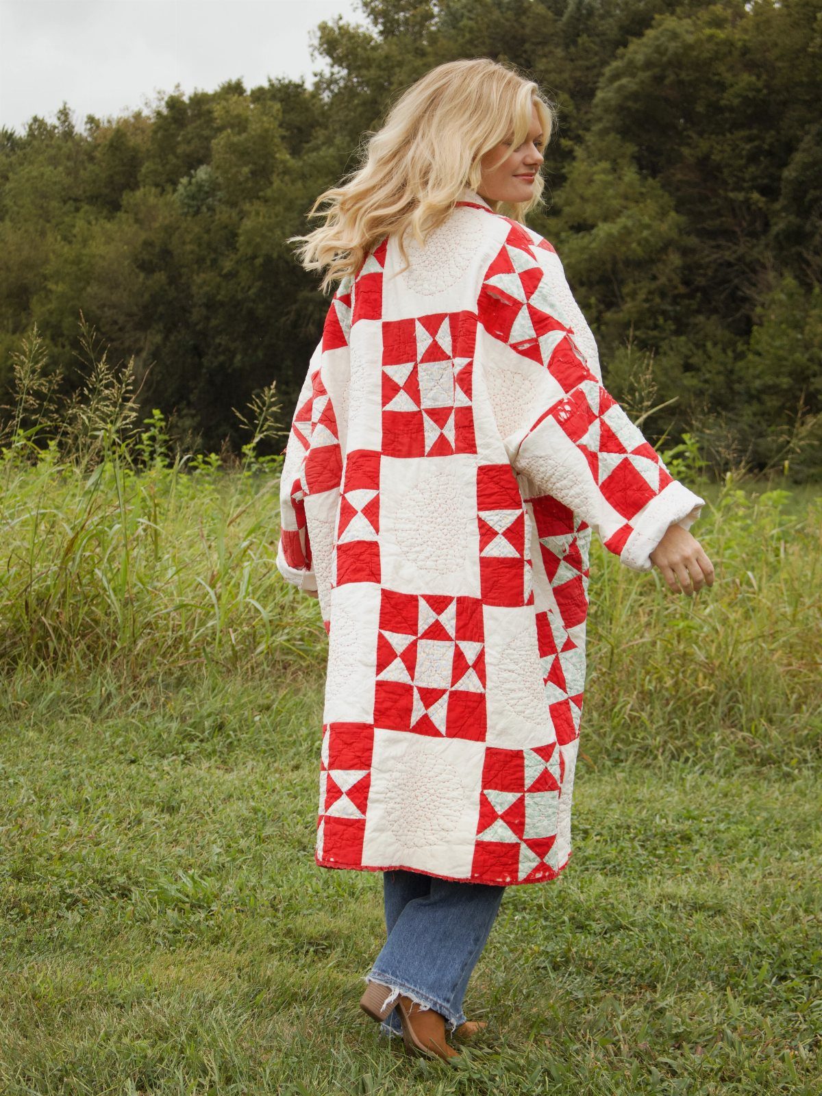 Woman wearing a long red and white patchwork quilted jacket in a grassy field.
