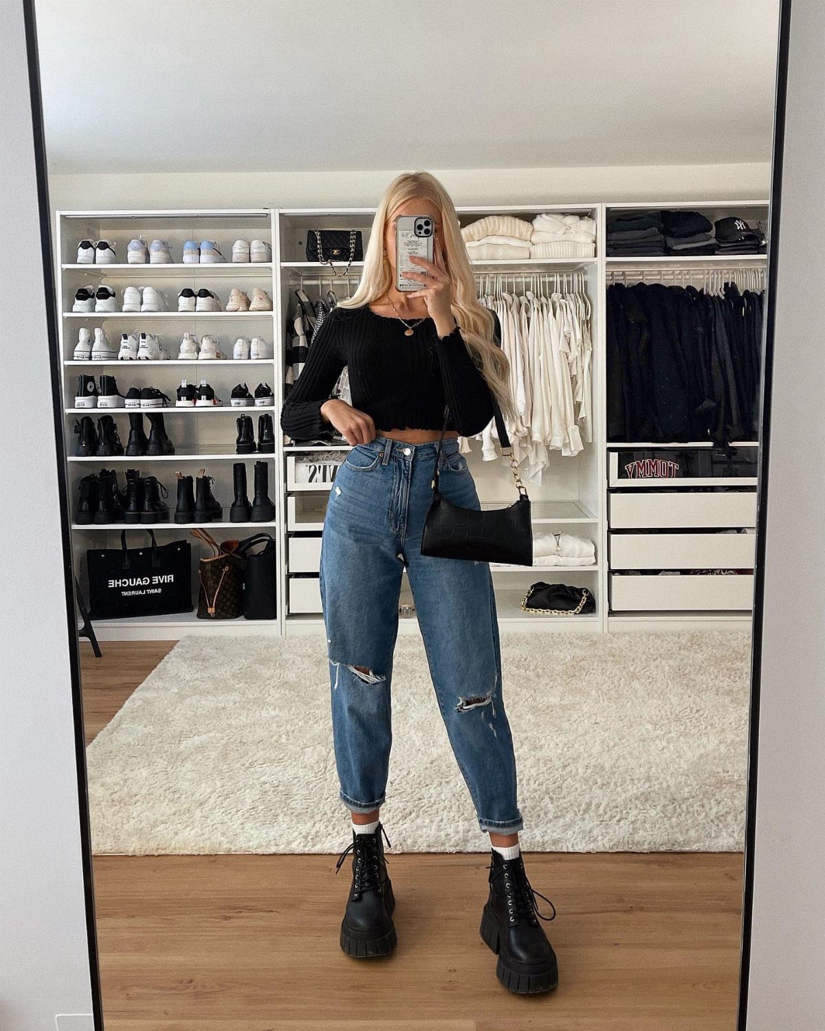 Woman wearing blue ripped mom jeans, black cropped top, and black chunky ankle boots.