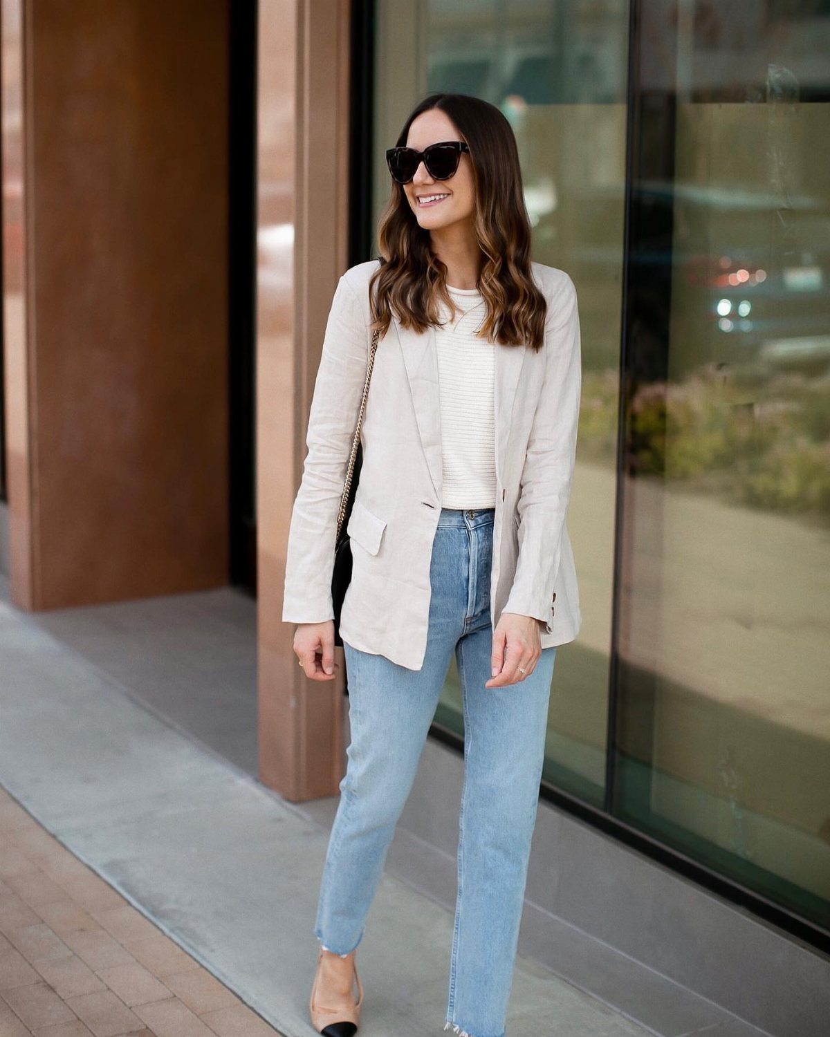 A woman wearing light blue mom jeans, a beige blazer, and tan high heels.