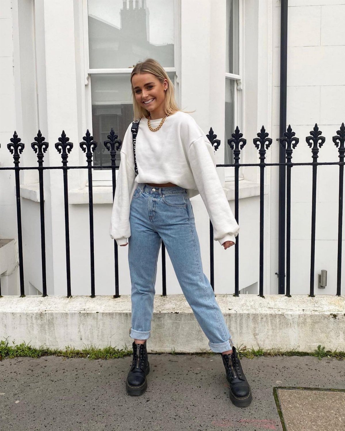 A woman wearing a white oversized sweater and light blue mom jeans with black boots.