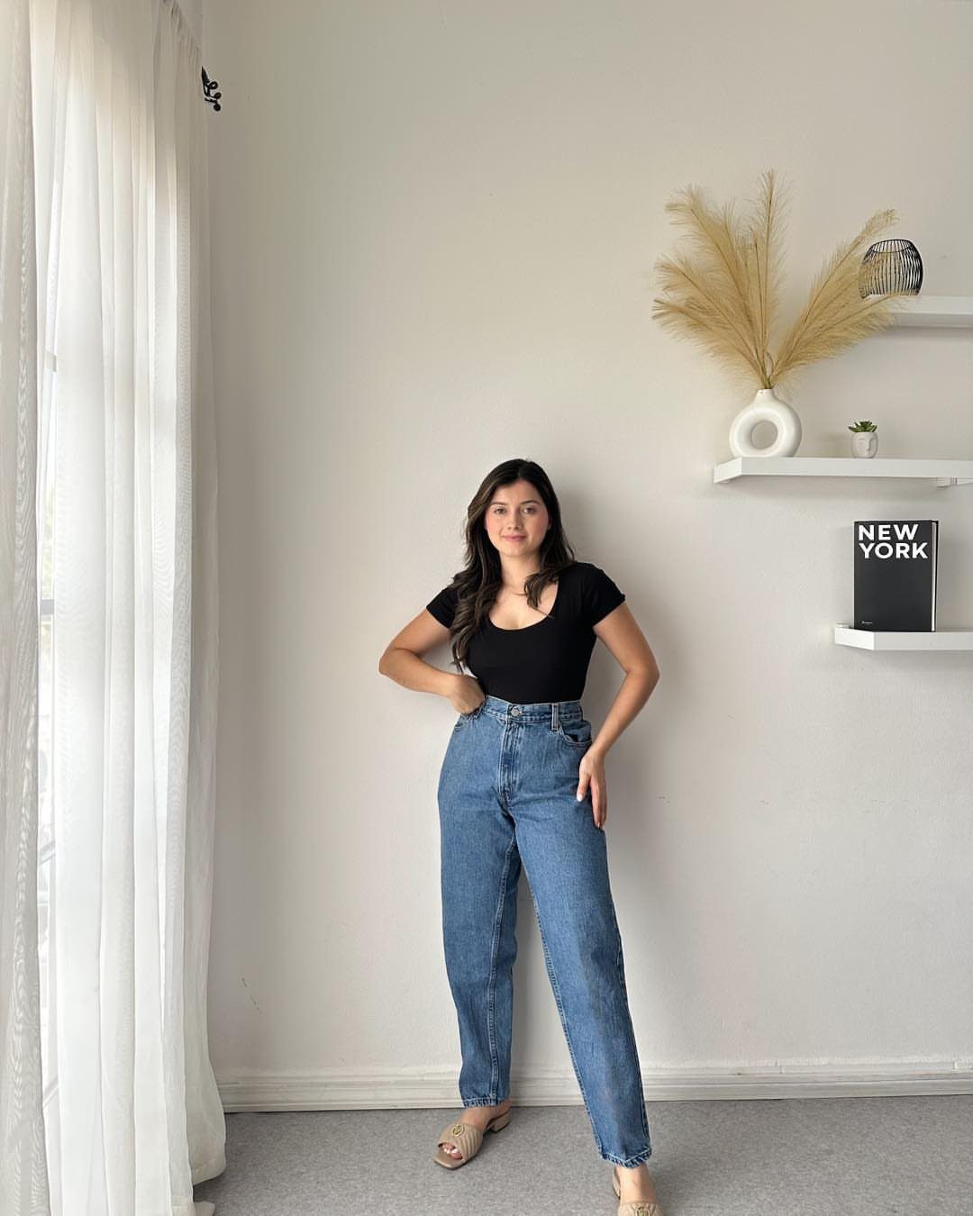 Woman wearing a black bodysuit tucked into high-waisted blue mom jeans and beige sandals.