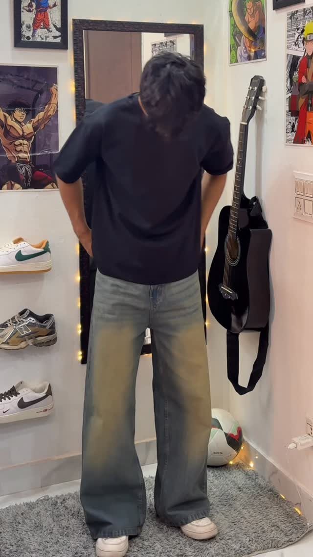A person wearing a black t-shirt and baggy blue jeans standing in a room.