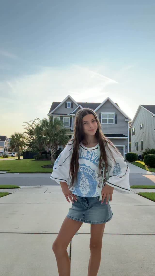 A teenage girl posing in an oversized white graphic t-shirt and a denim mini skirt.