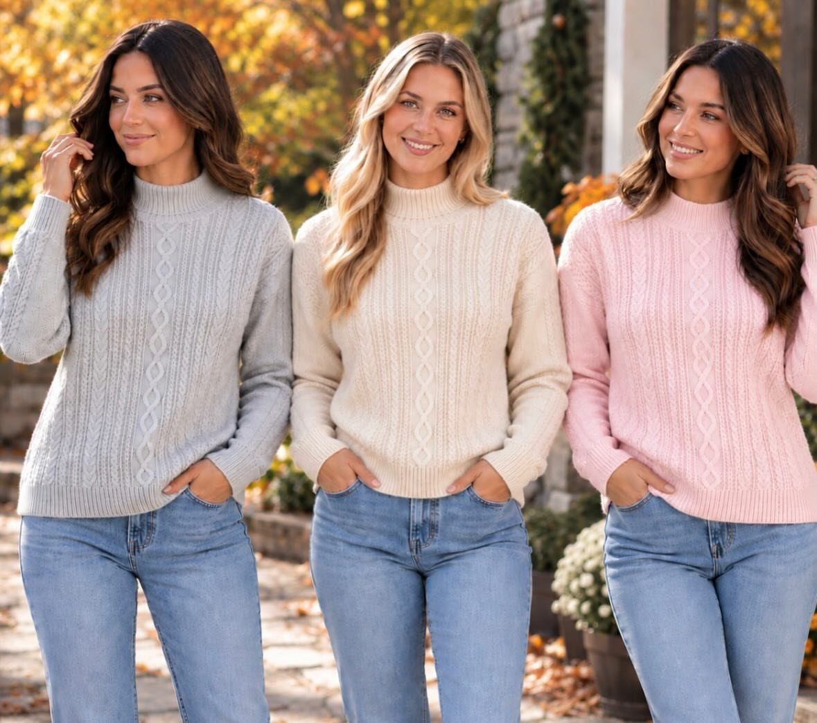 Three women smiling while wearing colorful cable-knit sweaters and blue denim jeans outdoors.