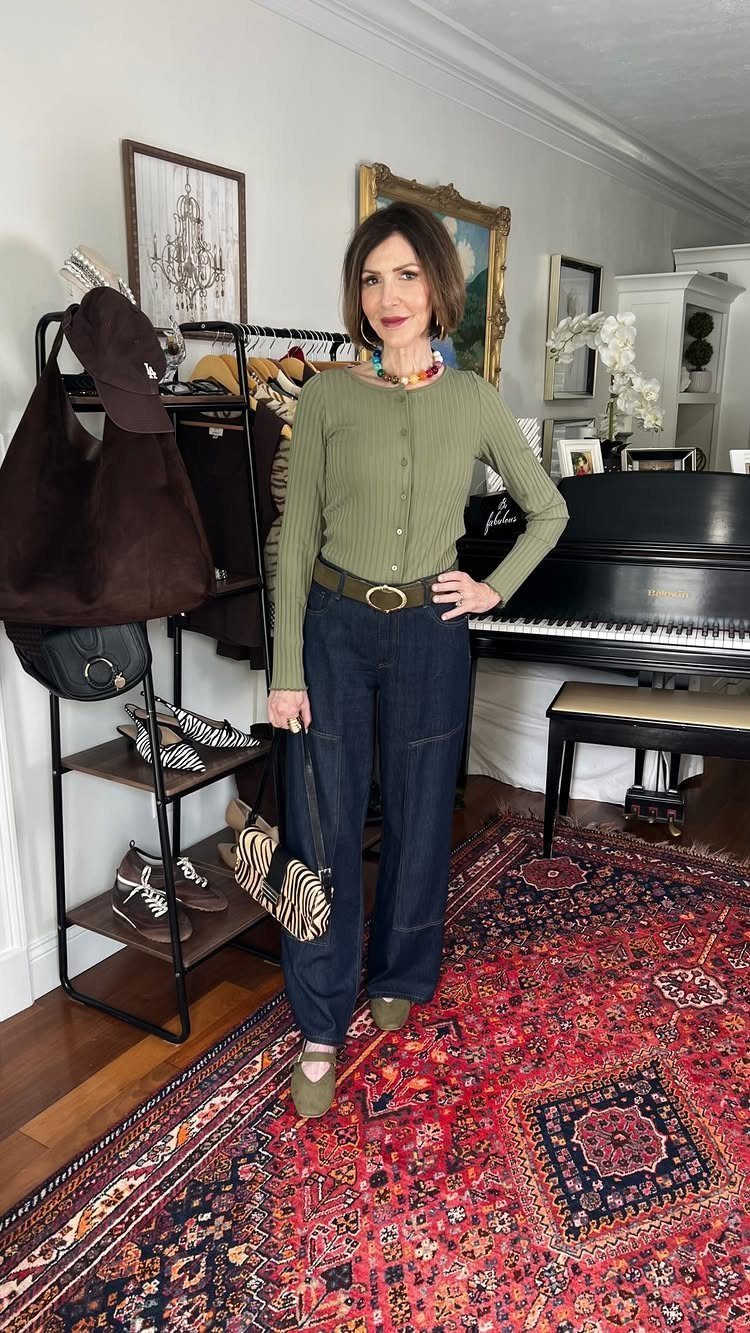 Woman in olive cardigan and dark blue wide-leg trousers standing on a red patterned rug.