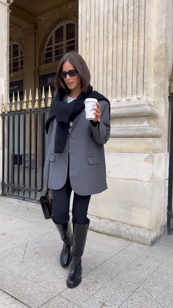 Woman walking in a city wearing a grey blazer, black leggings, and tall black boots.