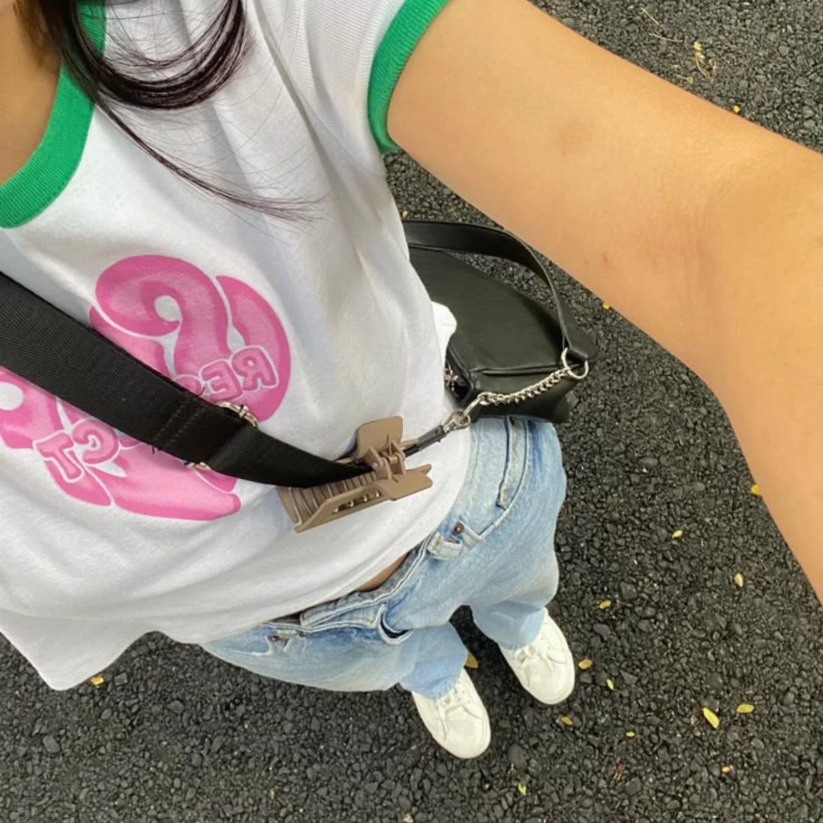 Person wearing a white graphic t-shirt, light blue jeans, and white sneakers on asphalt.