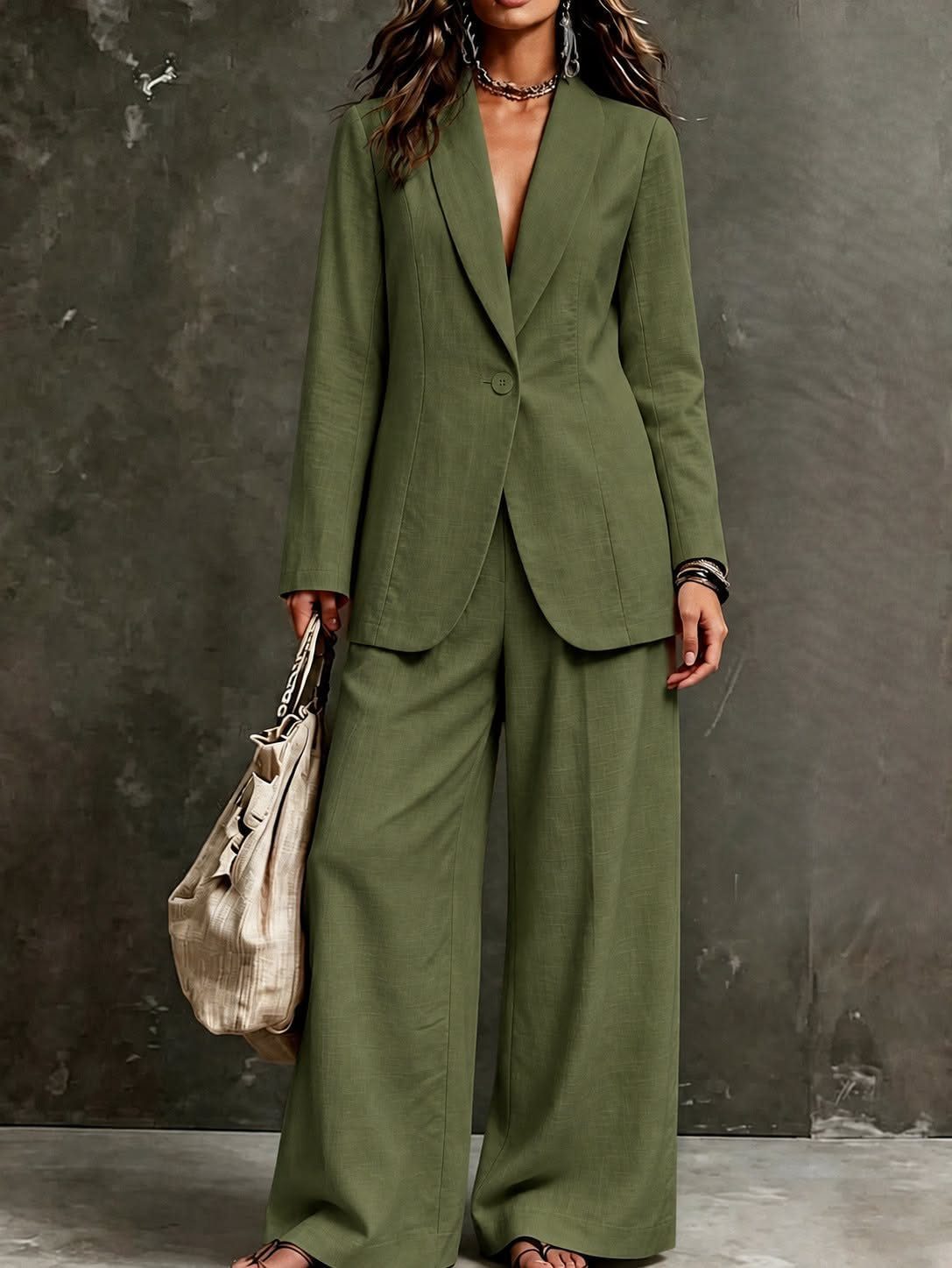 Woman wearing an olive green linen blazer and matching wide-leg trousers holding a beige bag.