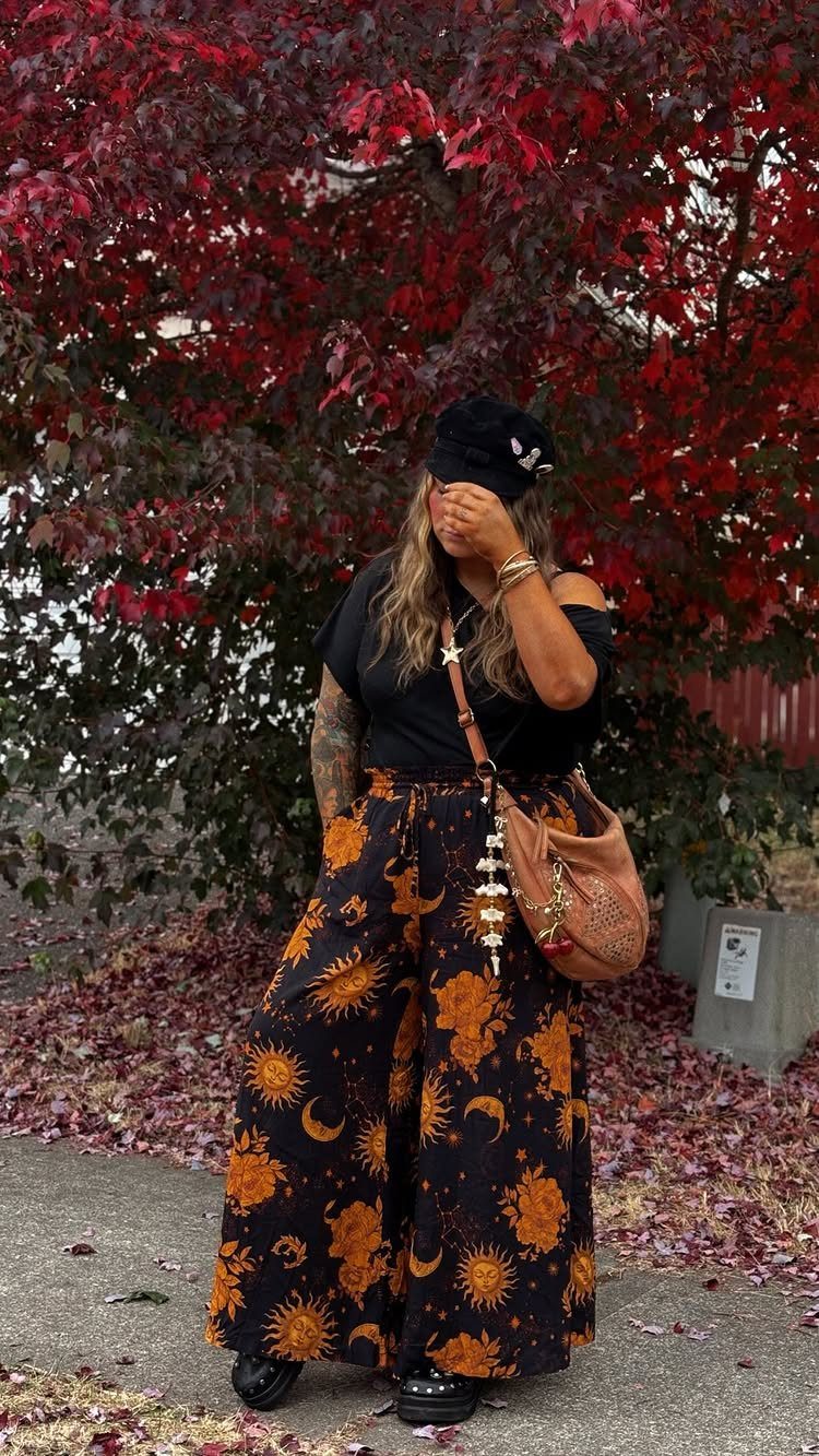 A person in celestial patterned wide-leg pants standing before vibrant red autumn leaves.