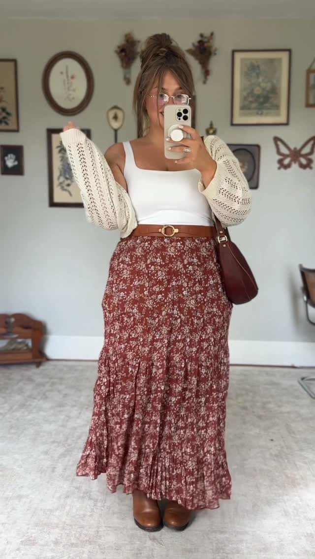 A woman posing in a white tank top, crochet cardigan, and long floral maxi skirt.