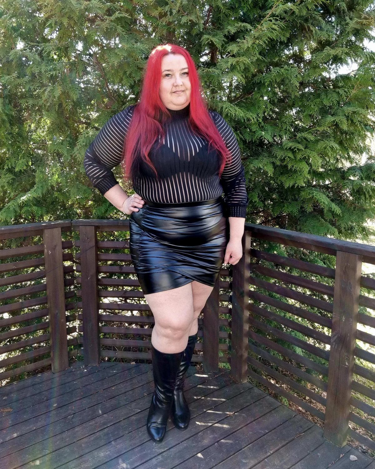 Woman with red hair wearing a black striped top, faux leather mini skirt, and black boots.