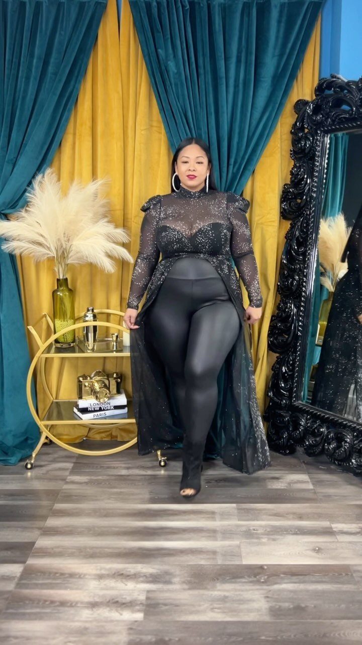 Woman in a black sequined long-sleeve top and black leggings posing in a decorated room.