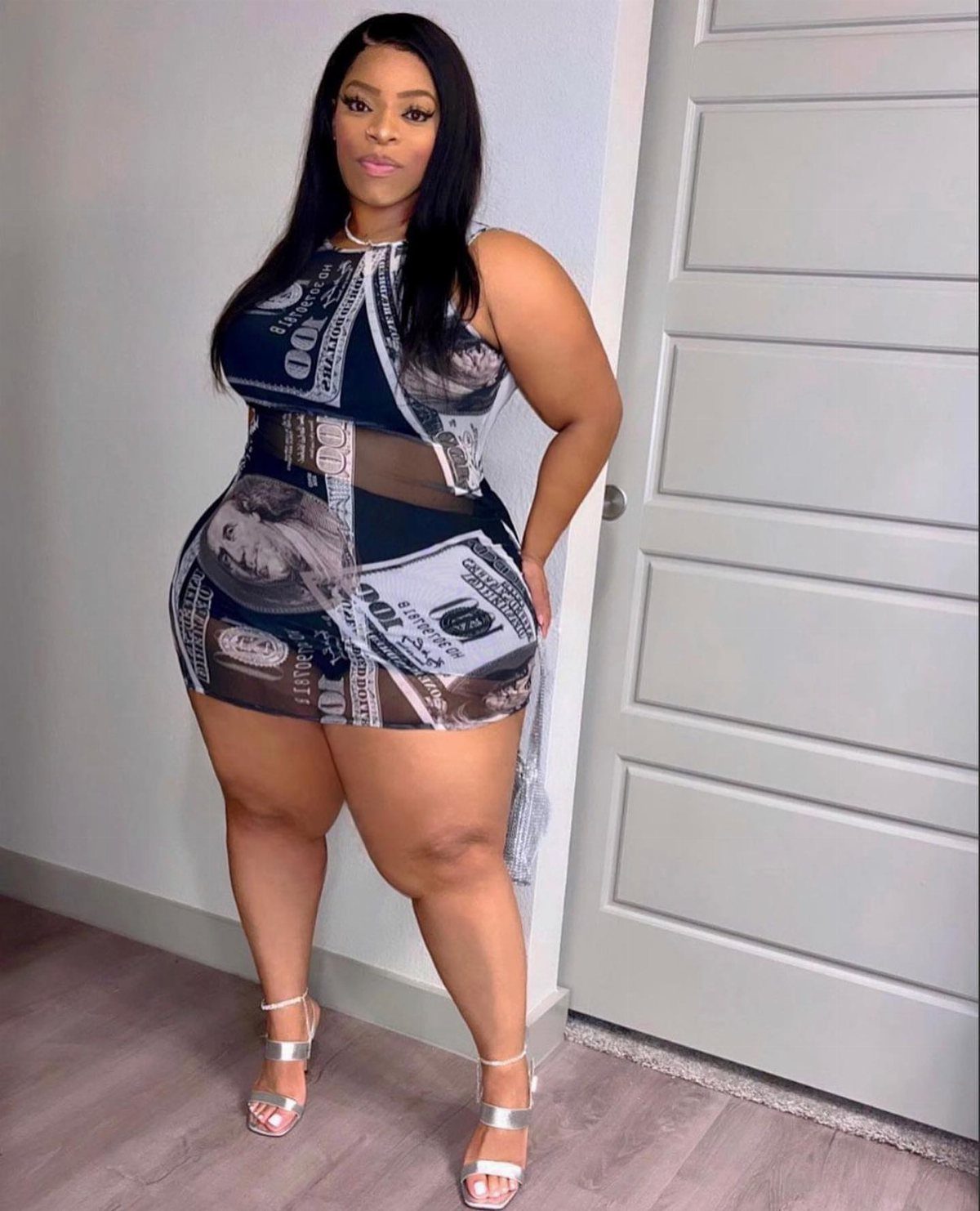 Plus size woman posing in a black and white dollar bill print mini dress.