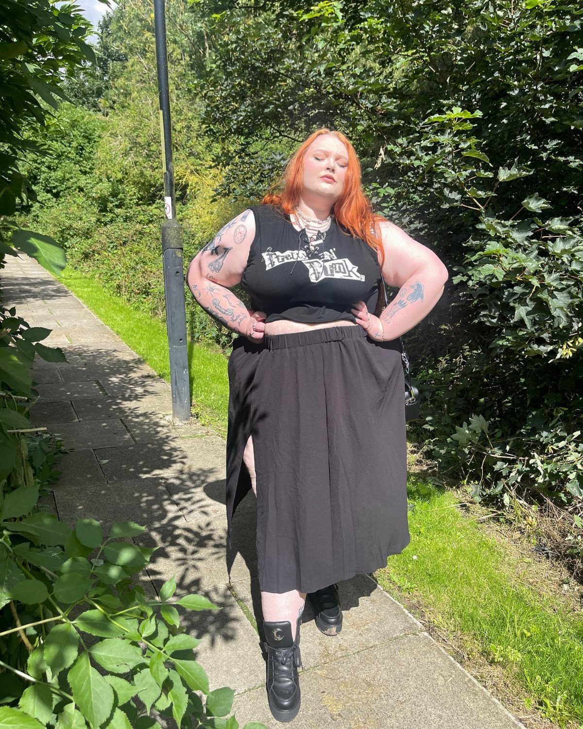 A plus-size woman with red hair wearing a black graphic tank top and long black skirt.