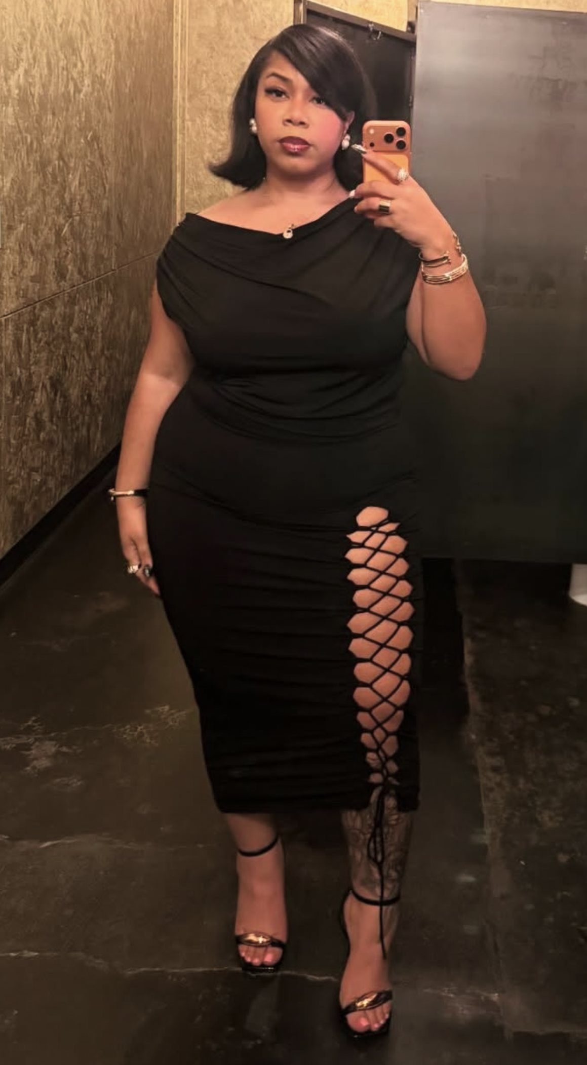 Woman posing in a black form-fitting midi dress with a lace-up side slit.