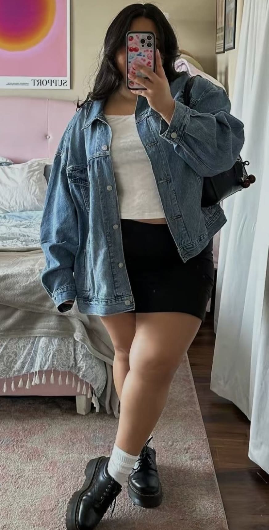 Woman in an oversized blue denim jacket, white tank top, and black mini skirt.