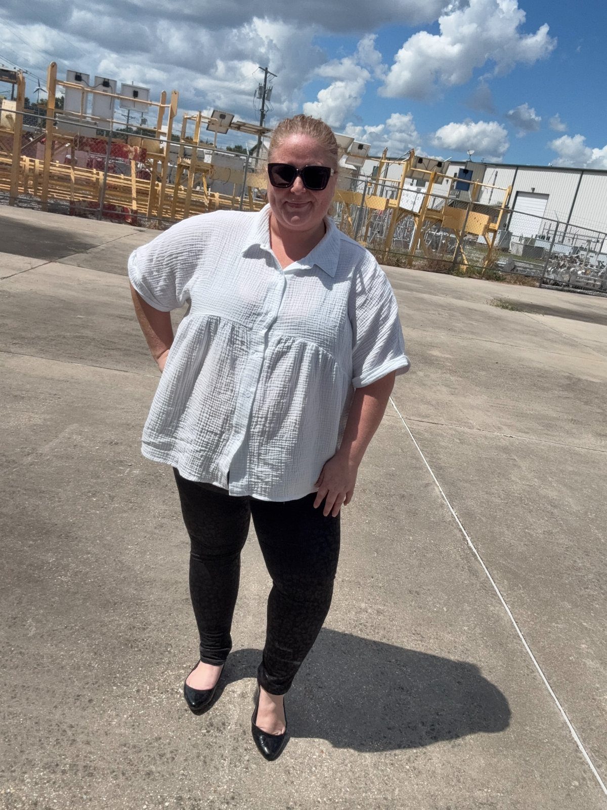 A woman in a white button-down shirt and black leggings standing outdoors on concrete.