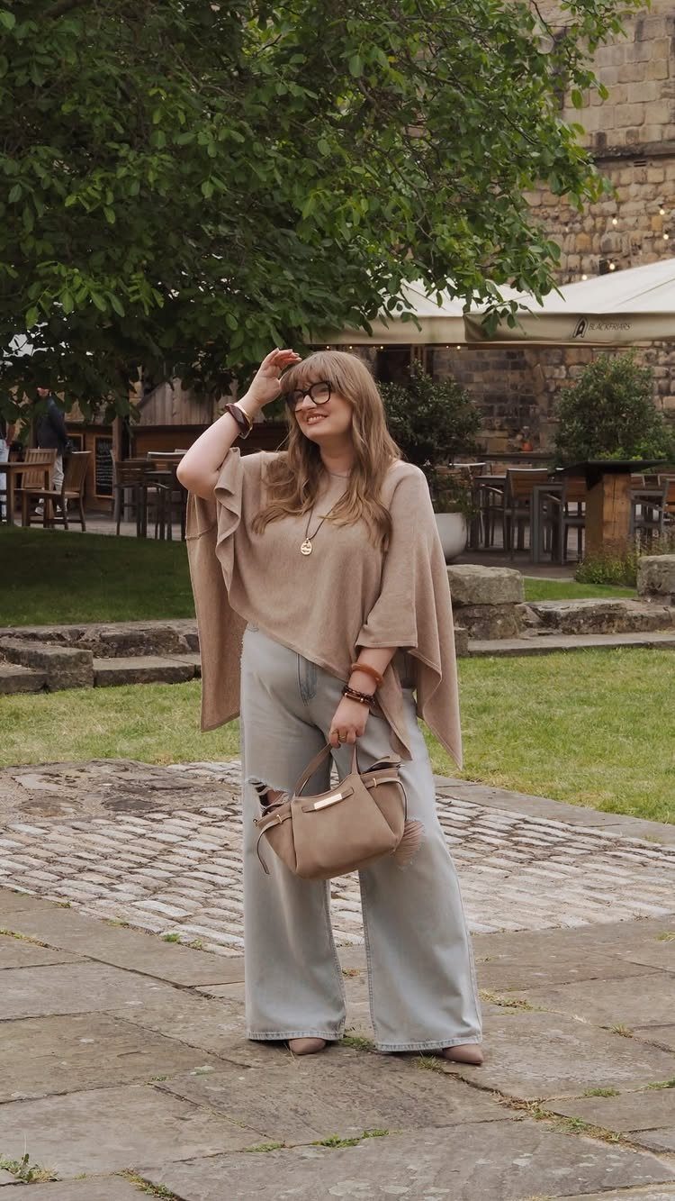 A woman wearing a beige top and wide-leg jeans posing in an outdoor courtyard.