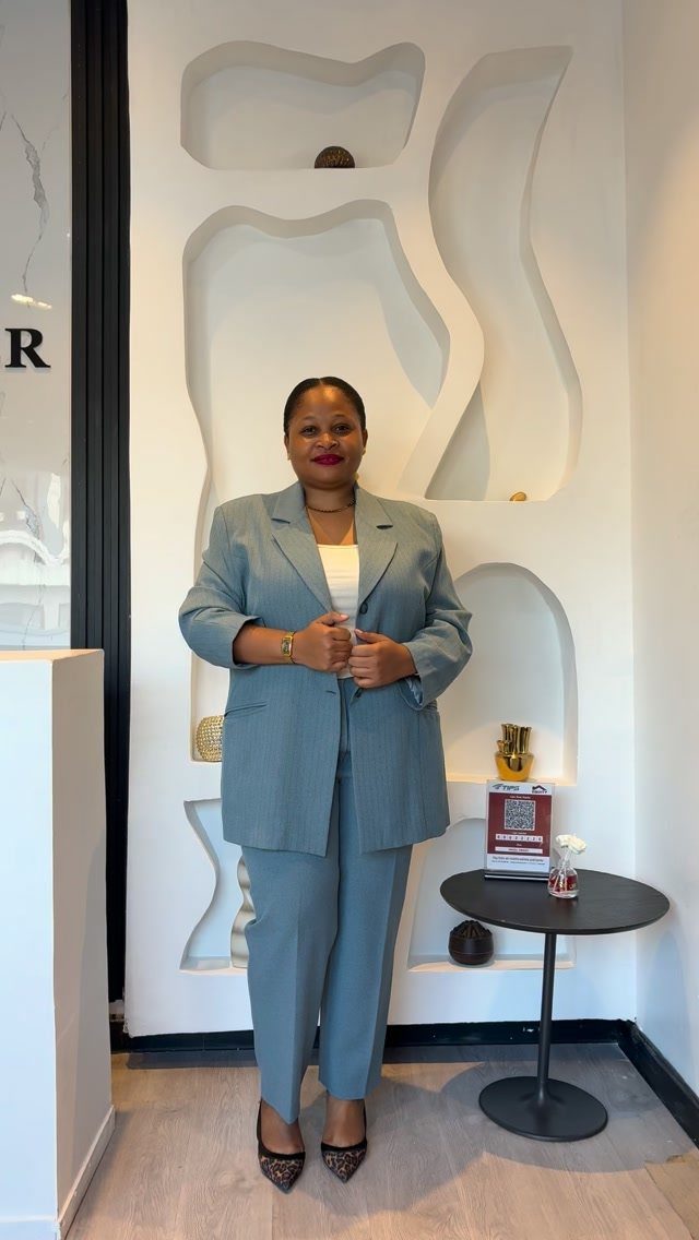 A woman posing in a light blue blazer and matching trousers in a modern room.