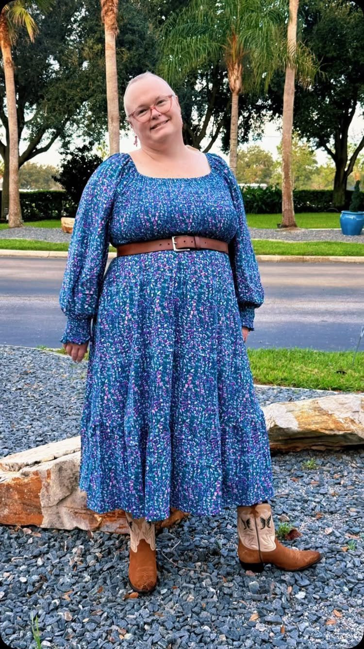 A woman in a blue floral dress and brown leather cowboy boots standing outdoors.