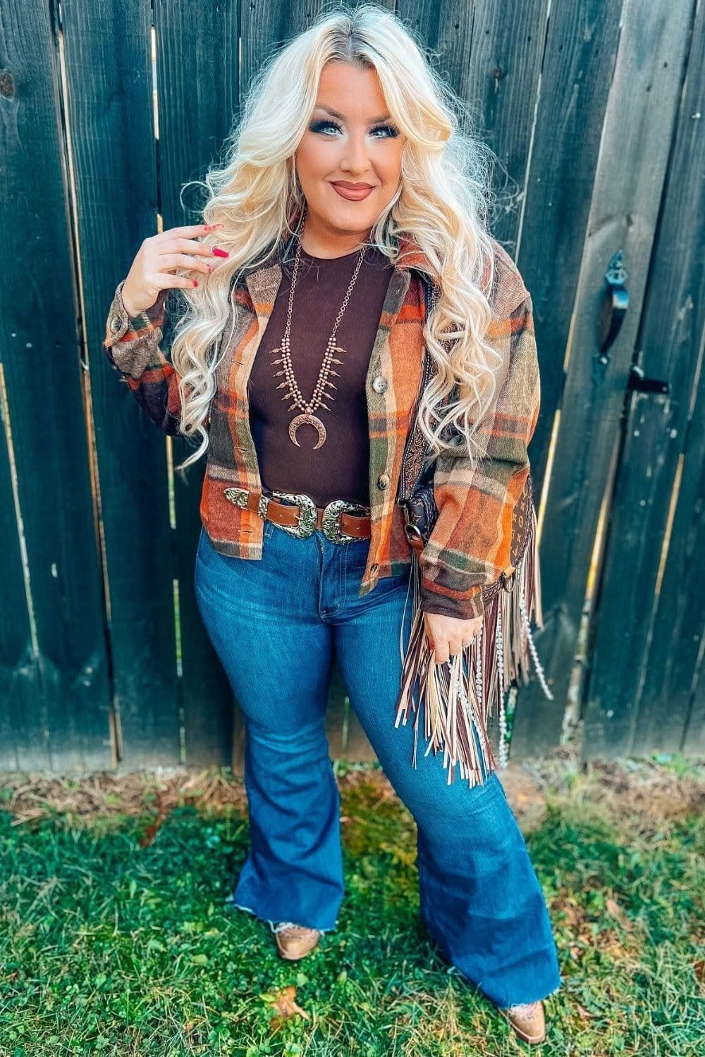 A blonde woman wearing a brown plaid flannel shirt and blue flared jeans.