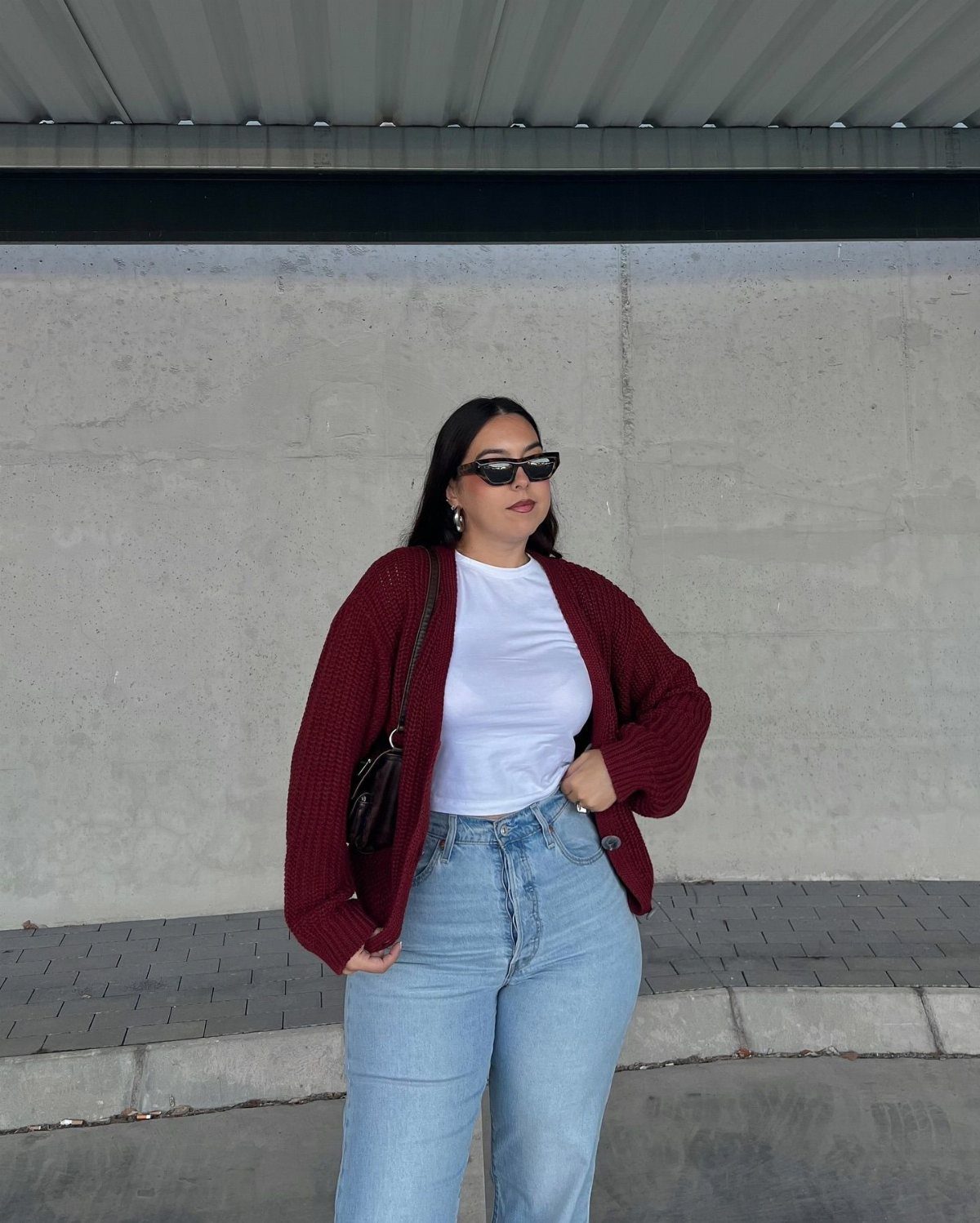 A woman wearing a burgundy ribbed cardigan, white t-shirt, and light blue jeans.