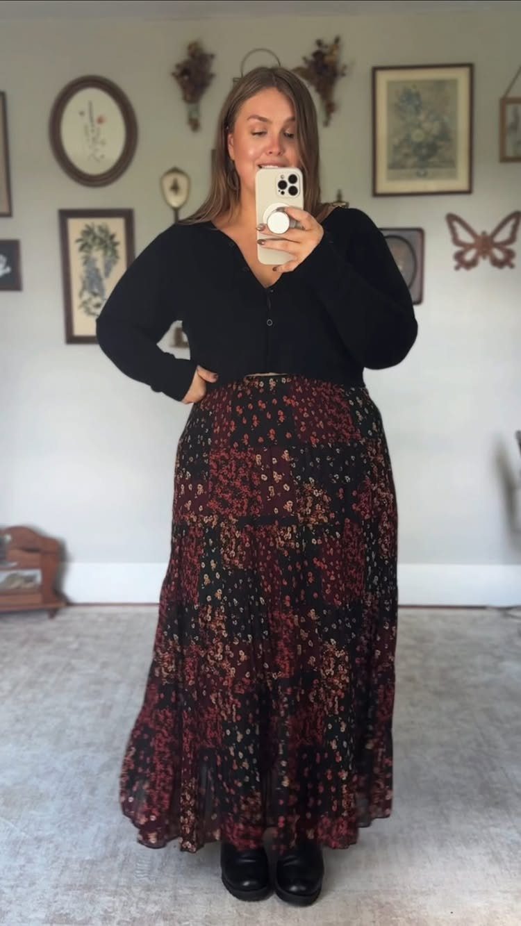 Woman in a black cardigan and red floral tiered maxi skirt posing for a mirror selfie.
