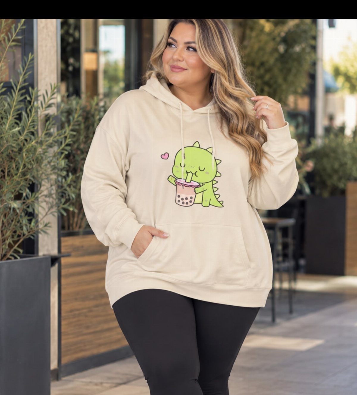 A woman in a cream graphic hoodie with a dinosaur print and black leggings.