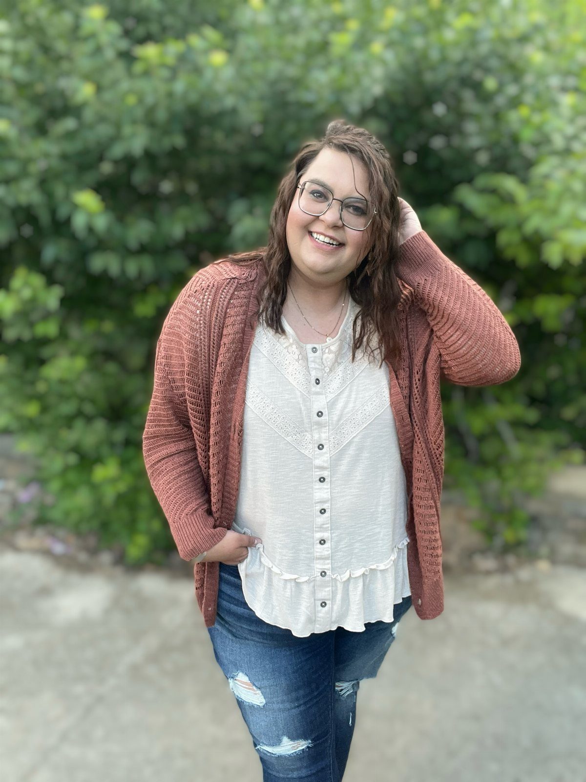 Smiling woman wearing a long rust orange cardigan, white top, and distressed blue jeans.