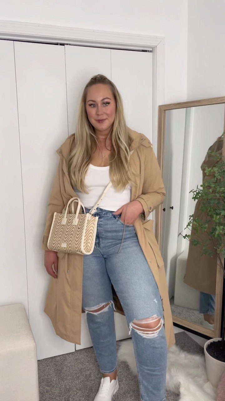 A blonde woman posing in a tan trench coat, white top, and ripped blue jeans.