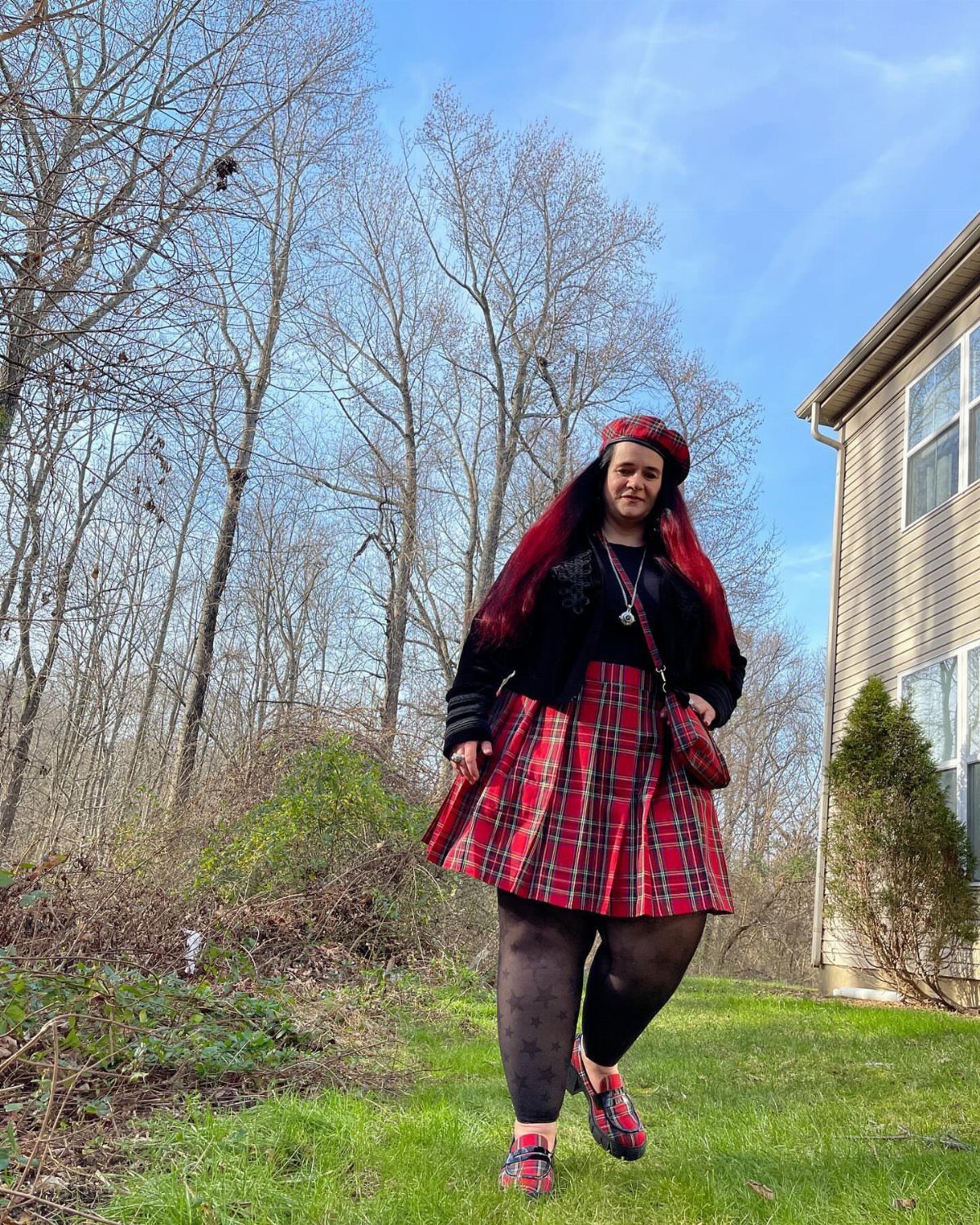A woman posing outdoors wearing a red and black plaid mini skirt and black top.