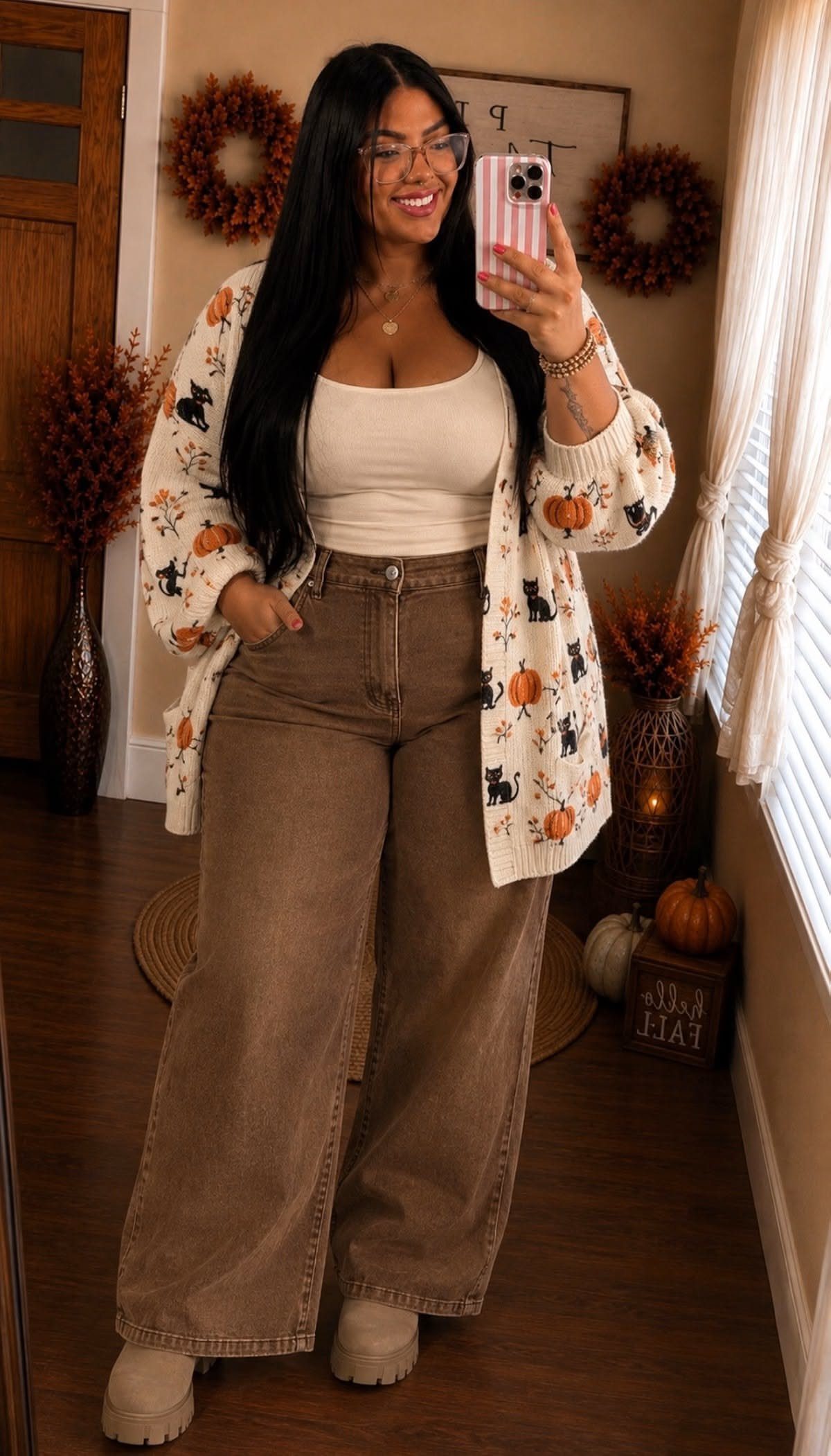 A woman posing in a mirror wearing a white pumpkin cardigan and brown wide-leg trousers.