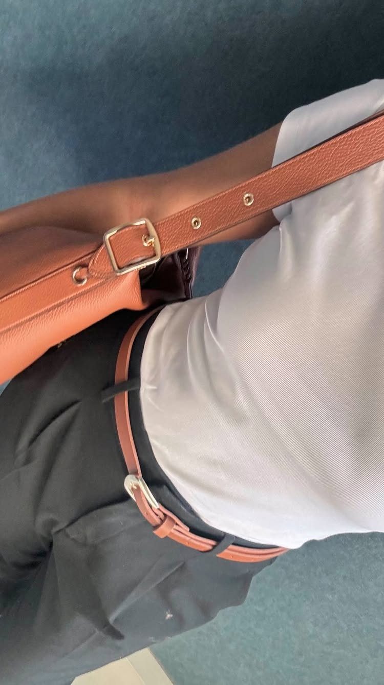 A person wearing a white blouse, black trousers, a brown belt, and a brown leather bag.