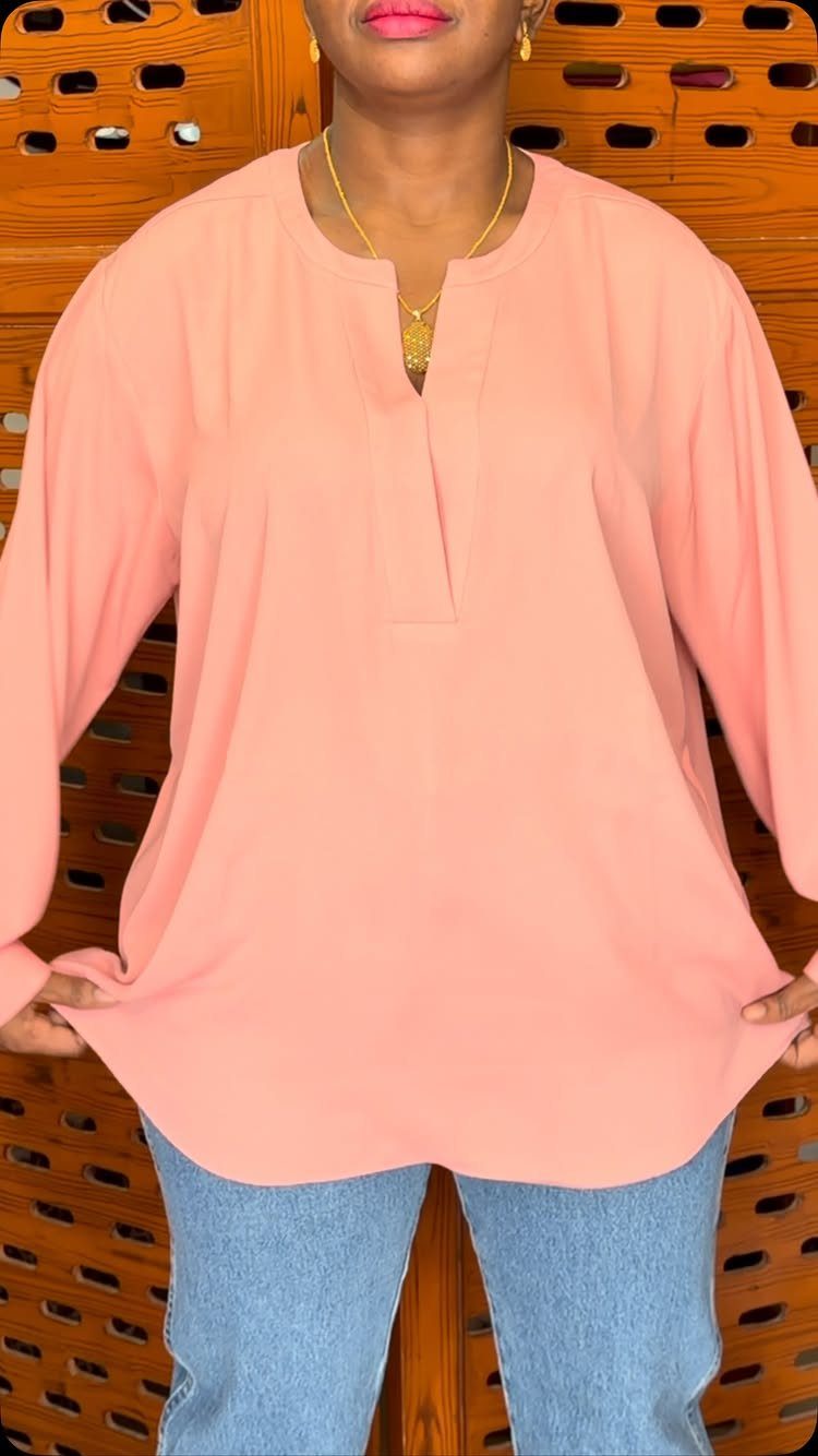 A person wearing a peach long-sleeved blouse and blue jeans against a wooden background.