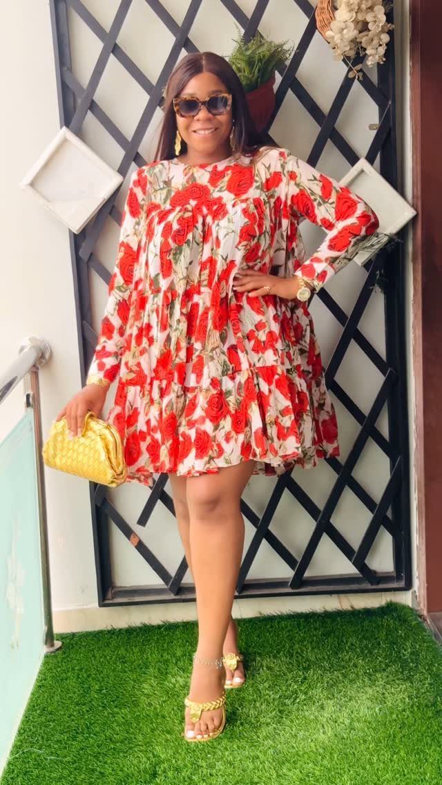 A woman posing in a red and white floral patterned short dress and gold accessories.