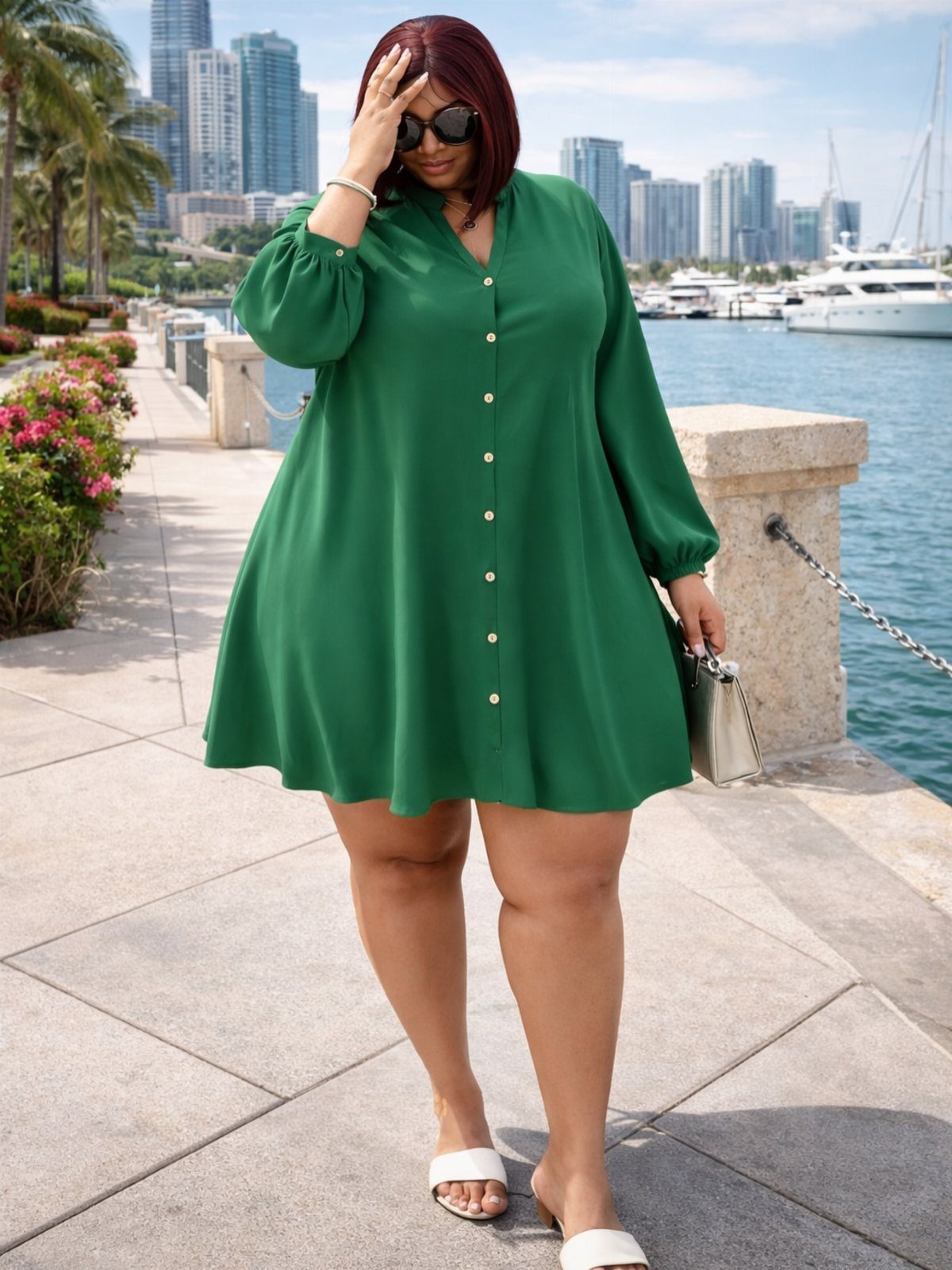 A woman wearing a green long-sleeved shirtdress and white sandals standing by a waterfront.
