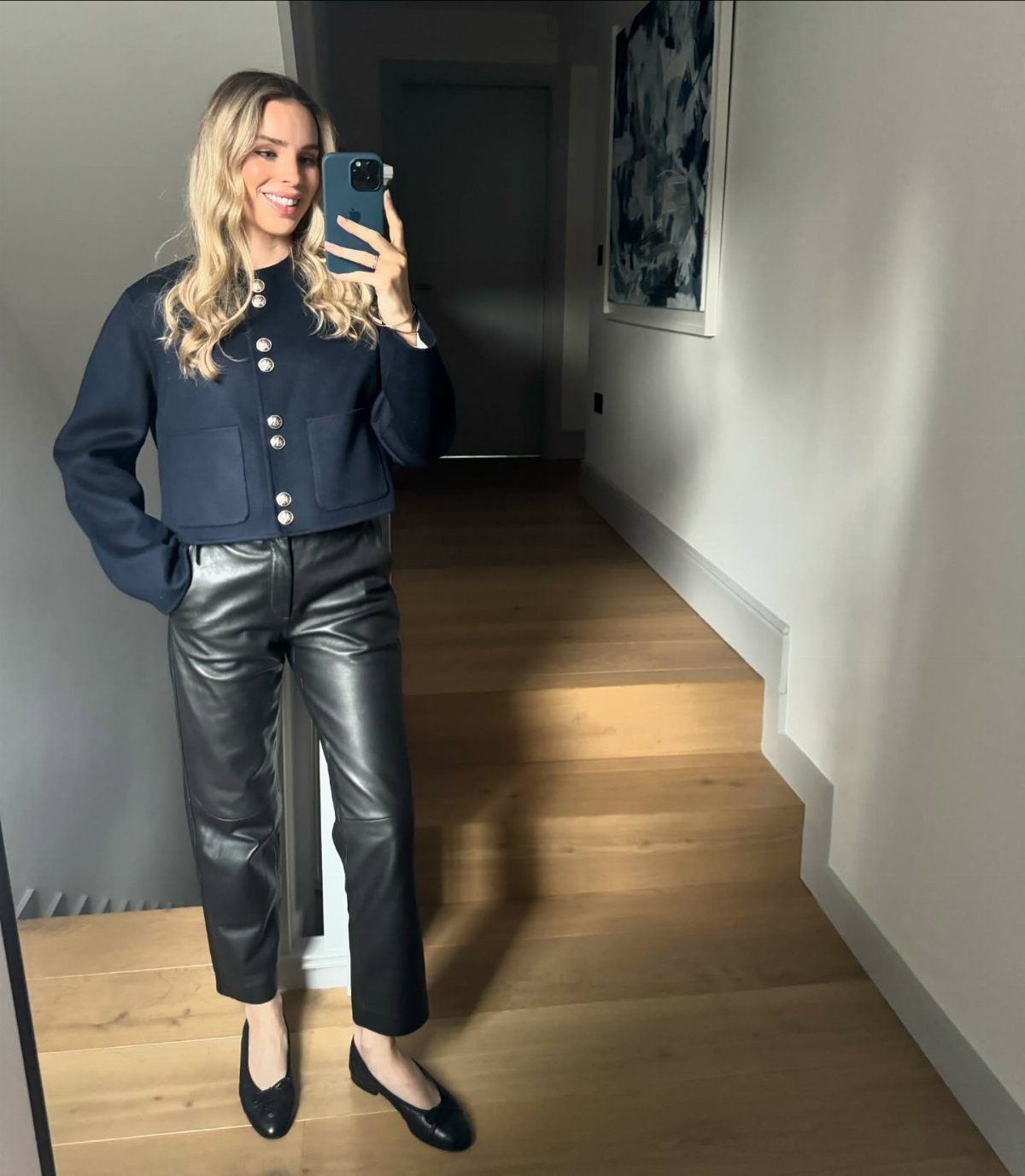 A woman posing in a navy jacket, black leather pants, and ballet flats.