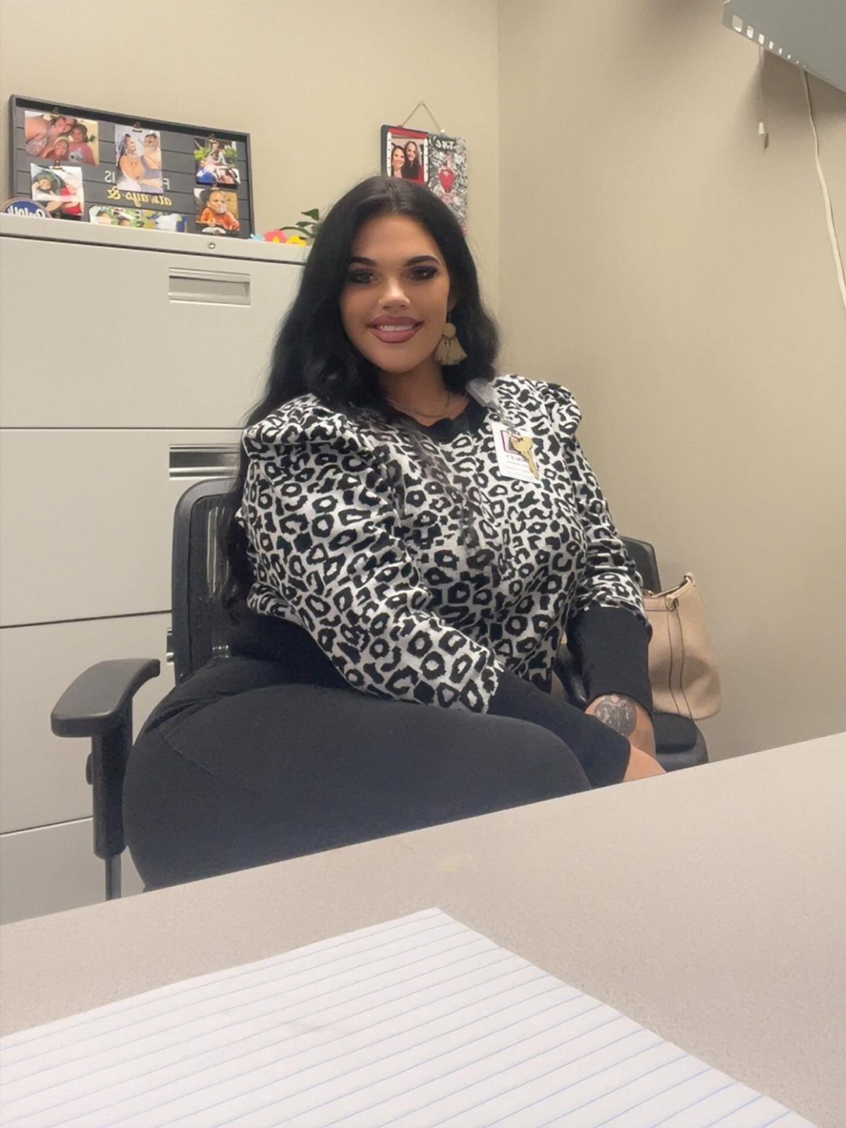 A woman wearing a leopard print blouse sitting in an office chair and smiling.