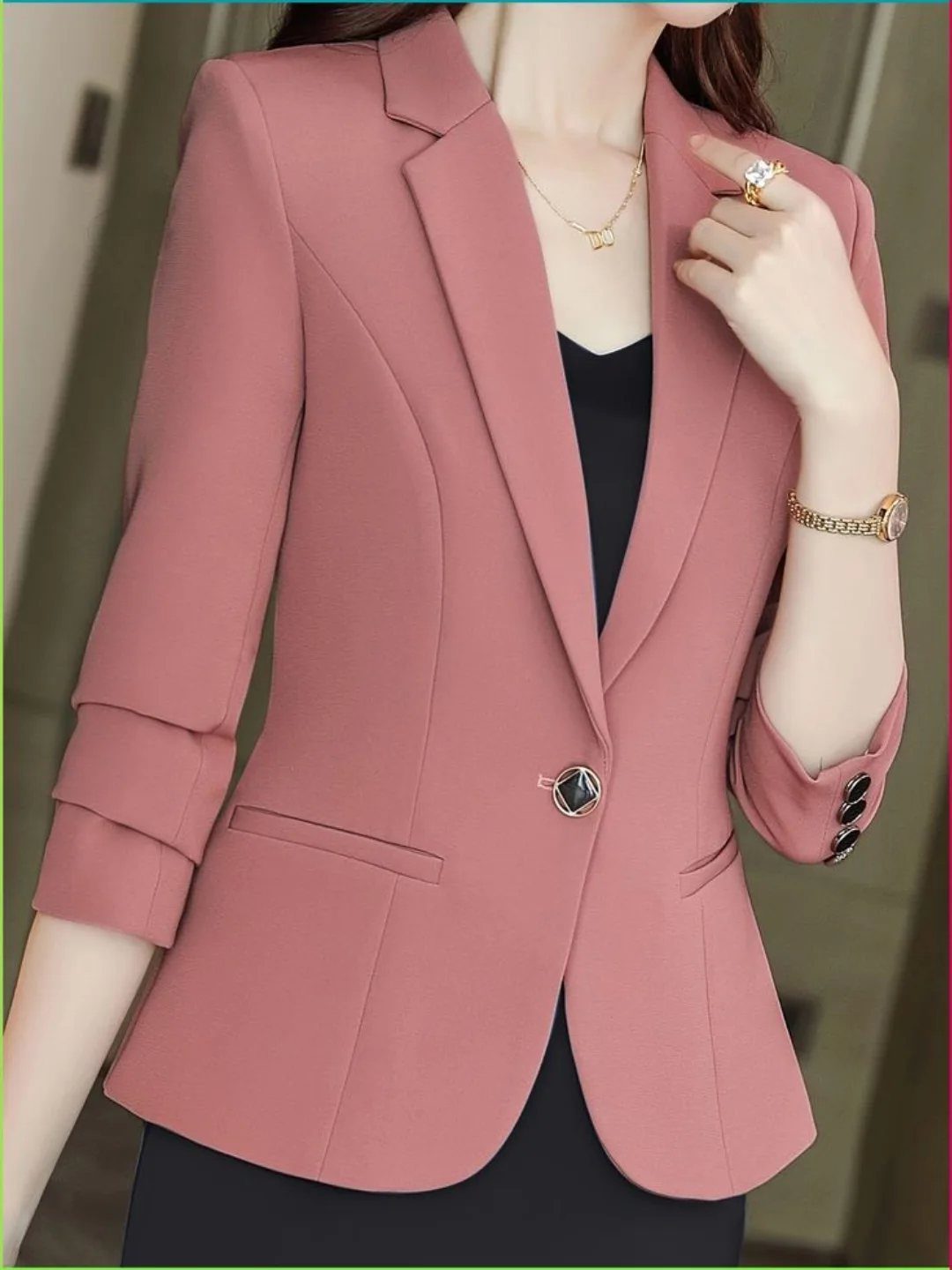 A woman wearing a dusty rose structured blazer over a black top and gold jewelry.