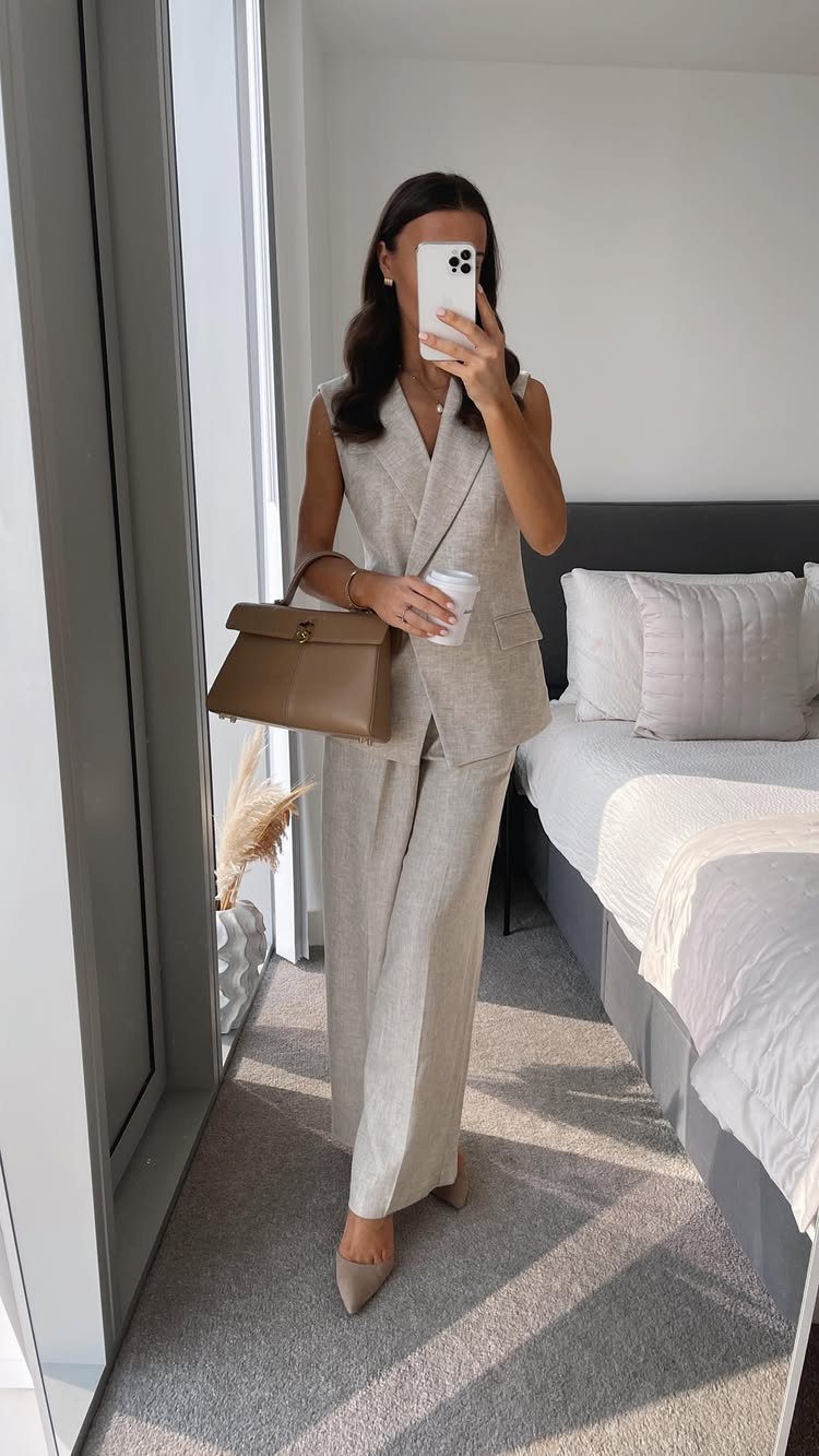 Woman wearing a beige linen vest and wide-leg trousers holding a handbag and coffee.