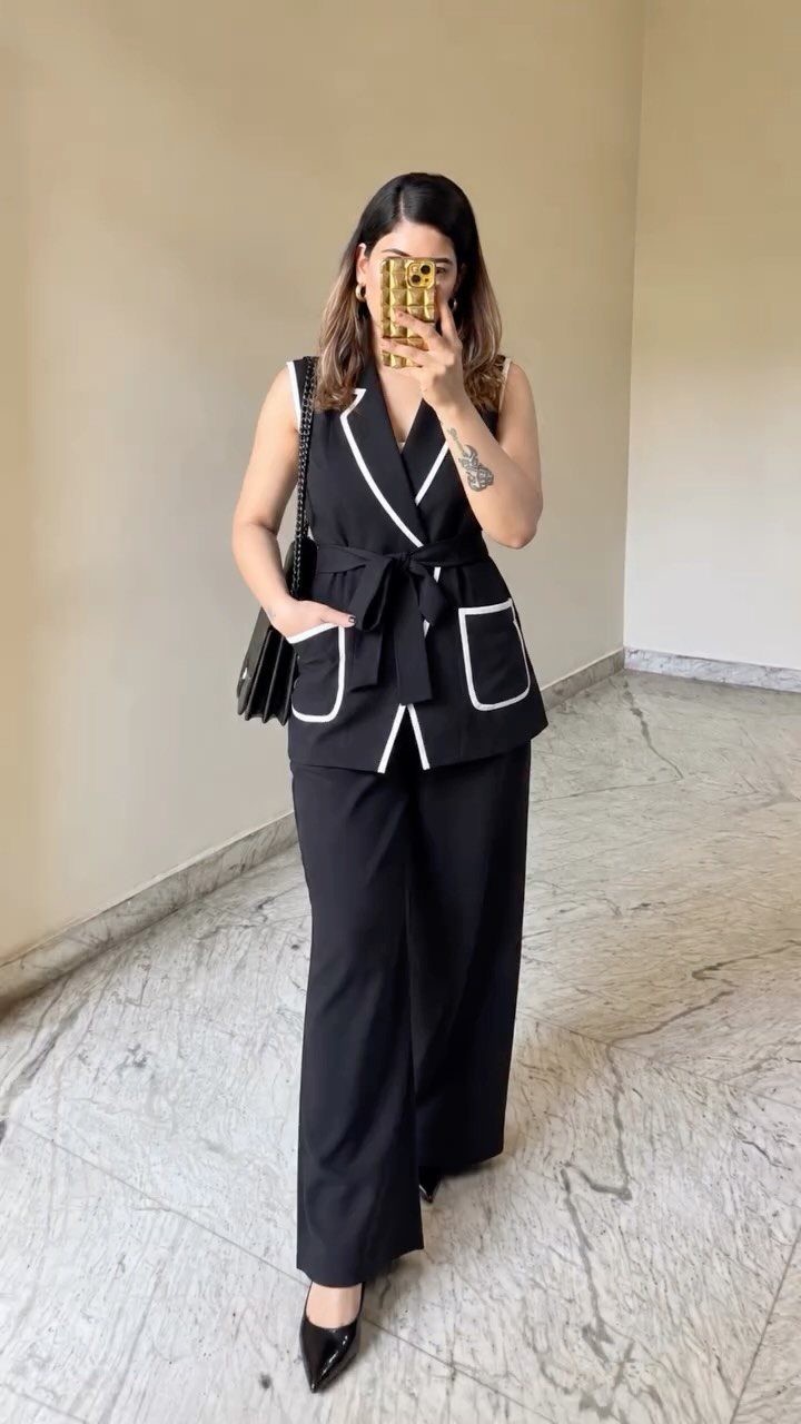 Woman in a black sleeveless vest and wide-leg trousers co-ord set taking a selfie.