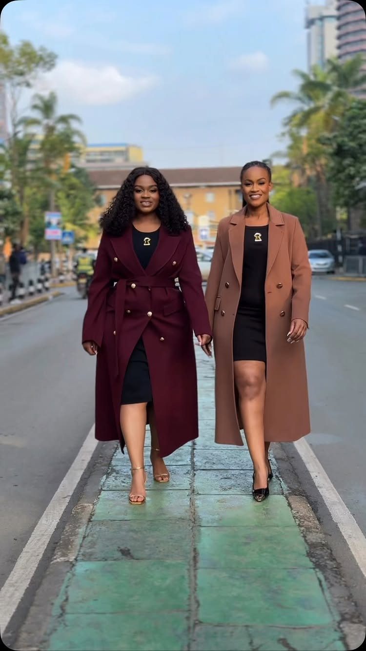 Two women walking outdoors wearing long, elegant wrap coats over black dresses.