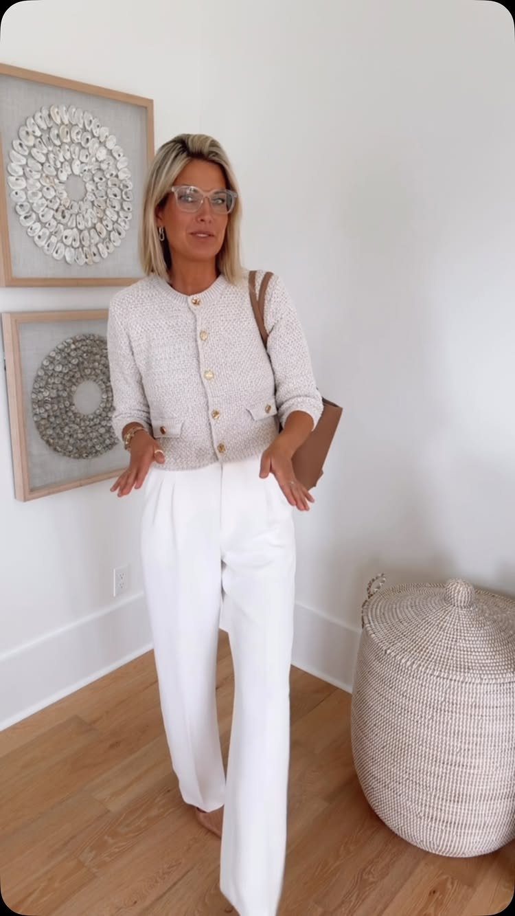 Woman wearing a beige cardigan and white high-rise wide-leg trousers standing in a room.