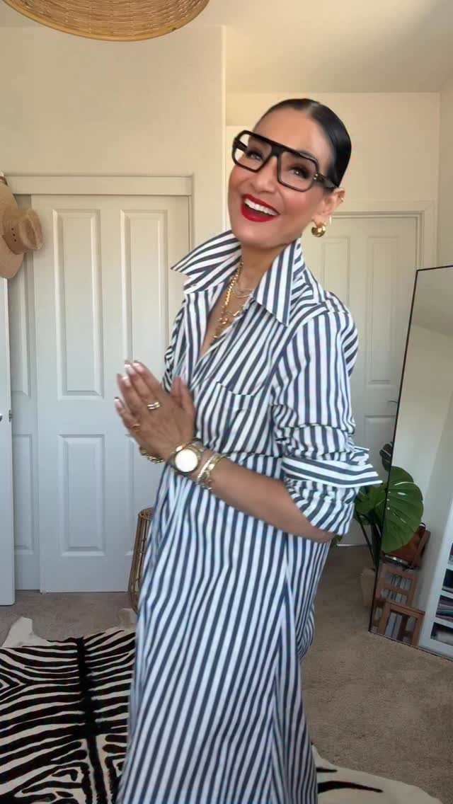 A smiling woman wearing a blue and white striped shirt dress and large black glasses.