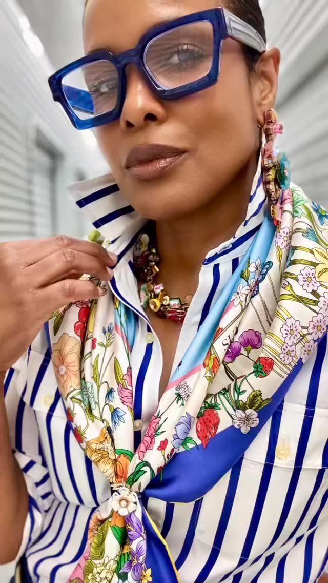 Woman wearing blue glasses and a colorful floral silk scarf over a striped shirt.