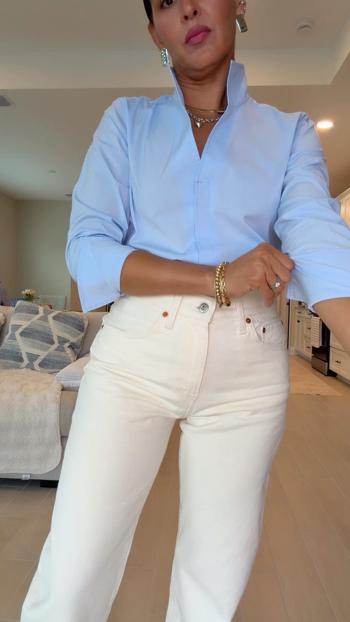 A woman wearing a light blue blouse and white jeans standing in a room.