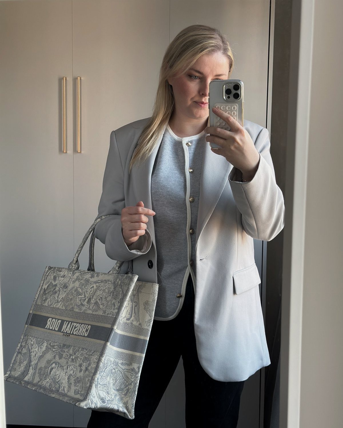 A woman in a light blue blazer and top holding a large patterned tote bag.