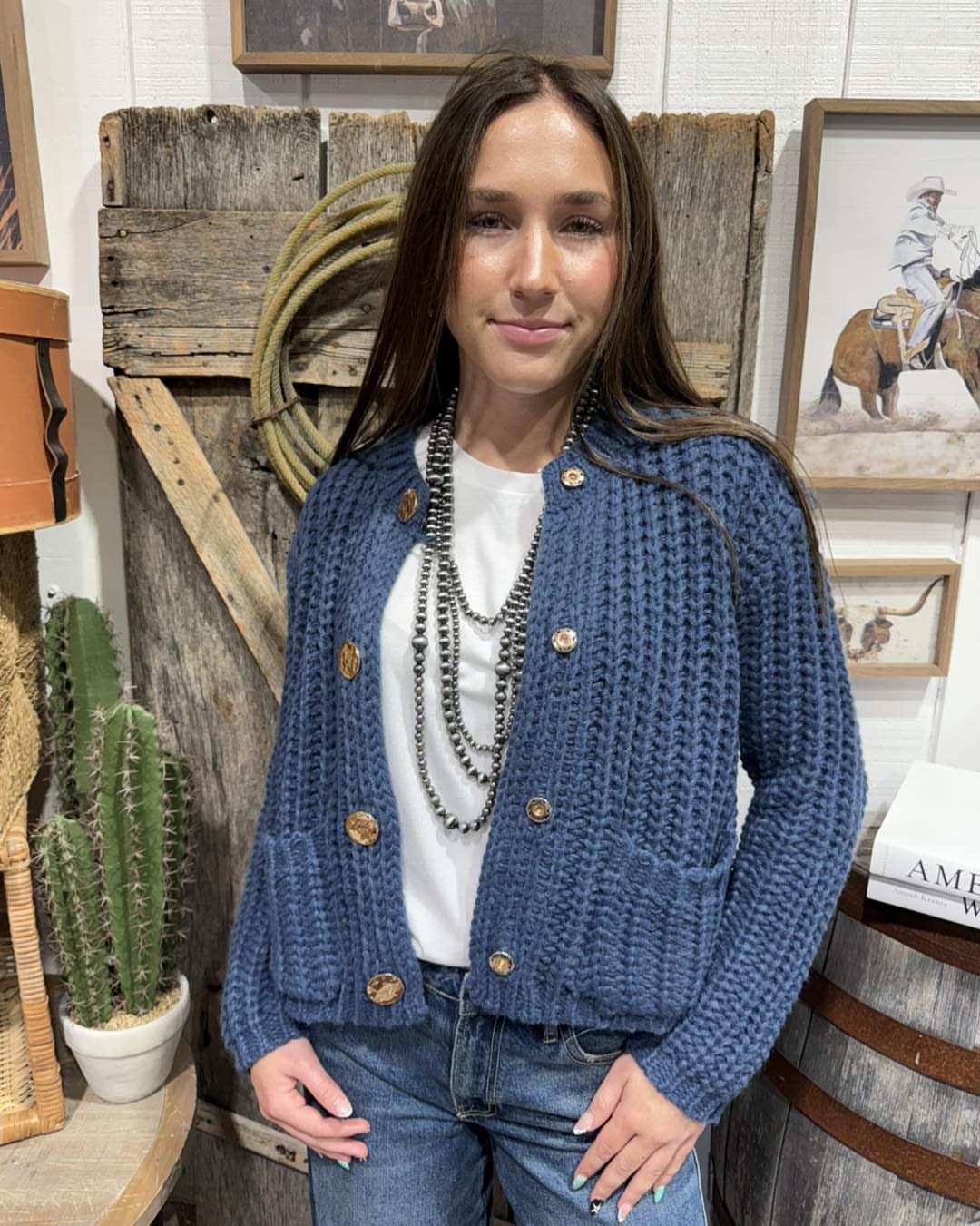 Woman wearing a blue chunky knit cardigan and blue denim jeans standing outdoors.